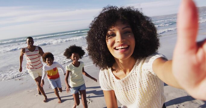 Running woman wearing knit top holding smartphone taking selfie on beach with footprints and waves - Powered by Adobe