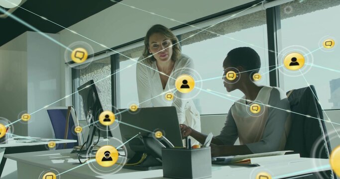 Collaborating two women in blazers leaning over laptop at office by window, with network overlay