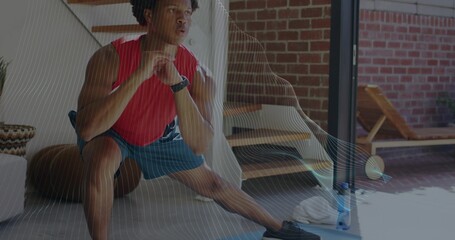 Performing man in red sleeveless top, blue shorts lunging in home with mat, water bottle