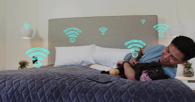 Reclining man petting dog in bedroom, wearing light blue tee, phone and Wi-Fi graphics, copy space