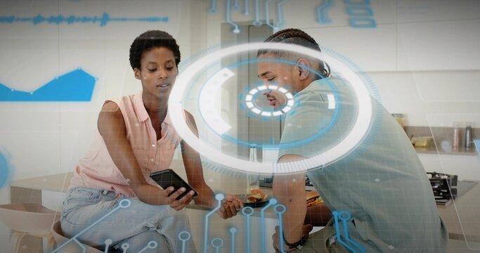 Sitting couple in kitchen, woman in pink blouse showing phone while man viewing AR HUD, pastries