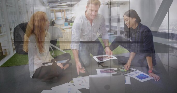 Reviewing printed mockups, three teammates sitting in office on carpet, with laptop and tablet