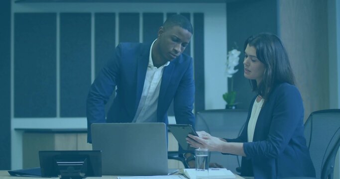 Reviewing mid adult colleagues wearing suits examining tablet in meeting room, with laptop, phone