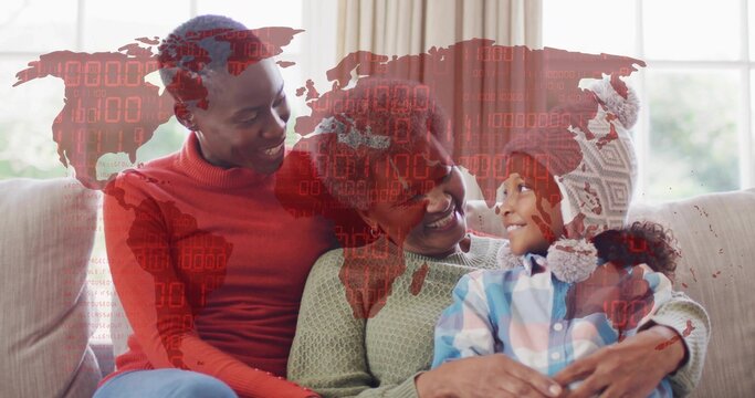 Hugging three-gen family wearing knit sweaters and pom-pom hat on light sofa, red world map overlay