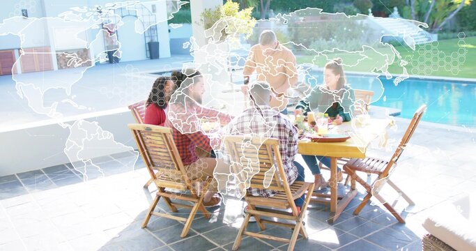Gathering six adults around wooden table sharing meal on tiled patio by pool, world map overlay - Powered by Adobe