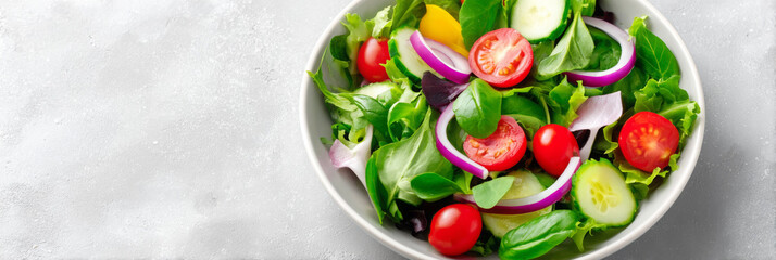 Fresh green salad with cherry tomatoes, cucumbers, red onions, and colorful peppers in a white bowl on a light gray background, showcasing healthy eating and vibrant colors