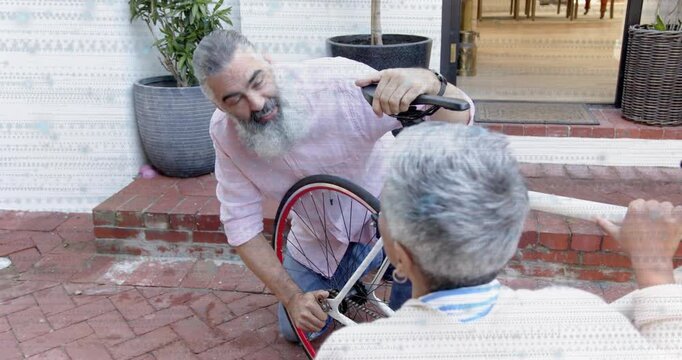 Bearded man spotting loose axle, kneeling, tightening wheel during repair, helper holding frame