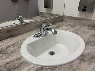 Clean modern restroom sink counter.Bright public restroom sink with chrome faucet and stone countertop, showing hygiene, cleanliness and contemporary facility design in a commercial interior space.