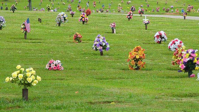 Row of Gravestones With Flowers at Cemetery. Grave Stones With Beautiful Flowers in Bright Sunshine. Memorial Park. Cemetery With Colorful Flowers on Graves. Death, Sadness, Sorrow and Loneliness.