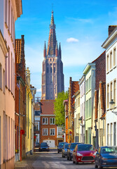 Bruges, Belgium. View at the Bell tower of church Our Lady in bruges old town. Narrow street with beautiful architecture and parked cars. Sunny summer day.