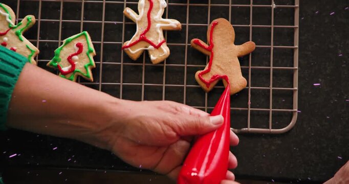 Female baker's hand entering with piping bag, outlining gingerbread man in red for festive baking