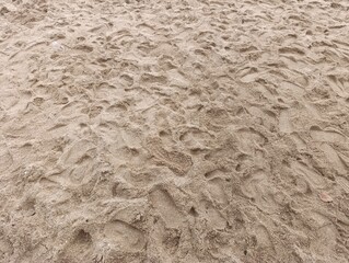 Textured brown beach sand covered with many fresh footprints. Close up of a sandy surface showing human activity and movement. Abstract natural pattern created by footprints walking on the shore.
