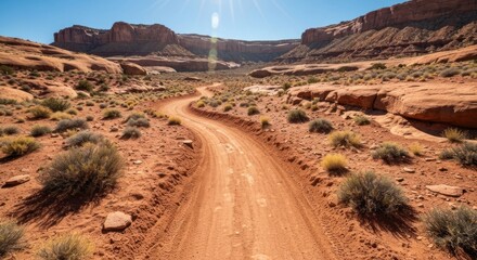 Fototapeta premium Dirt road winds through desert canyon, sun shining brightly overhead