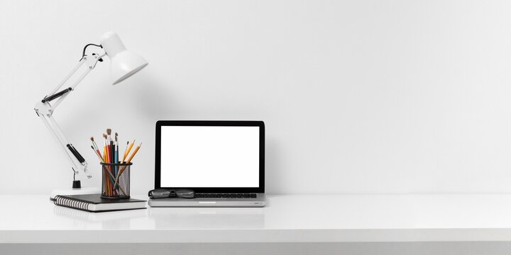 Minimalist desktop with laptop notebook lamp and stationery on clean white table