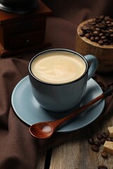 Aromatic coffee in cup, beans, brown sugar and grinder on wooden table, closeup