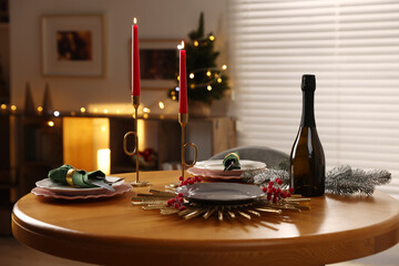 Christmas table setting with plates, wine and burning candles in festive decorated room