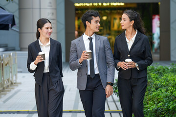 Diverse business team of Asian and Indian professionals walking and talking outdoors in modern city, holding tablet, coffee, and documents for outside meeting.