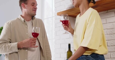 Couple drinking wine in glasses, talking romance. At home in a kitchen, they enjoy conversation, toasting with red wine as evening fills the room. Love, celebration and relationship concept. - Powered by Adobe