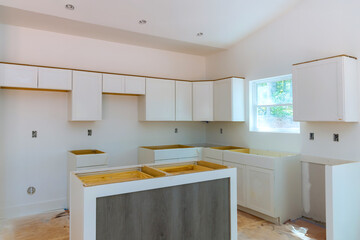 Workers are installing white kitchen cabinets preparing space for finishing touches in new home.