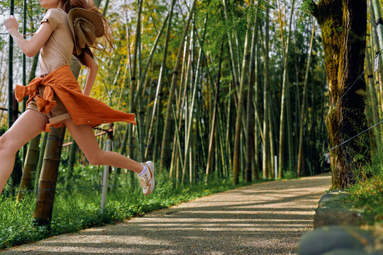 Girl jumping on a forest path with a backpack among tall bamboo, summer motion captured midair, carefree outdoor travel and energetic leap on a sunny nature trail. - Powered by Adobe