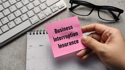 Business Interruption Insurance: Hand Holding Sticky Note with Text over Calendar and Keyboard for Corporate Risk Management