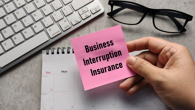 Business Interruption Insurance: Hand Holding Sticky Note with Text over Calendar and Keyboard for Corporate Risk Management