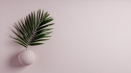 A single green palm leaf emerges from a textured, spherical vase, set against a soft, light pink background with subtle shadows. Minimalist, clean aesthetic.