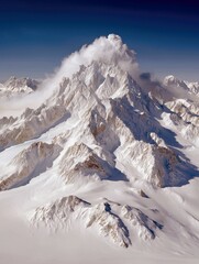 A majestic, snow-covered mountain range with sharp peaks and deep valleys, bathed in bright sunlight. Clouds drift around the highest summit, creating a dramati
