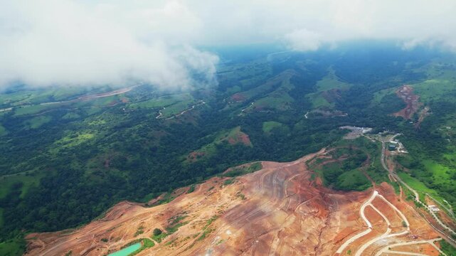 Towering aerial of Tandatangan Signature Golf Course in Mariveles, Bataan, rising above green fairways and winding roads with soft clouds drifting across the scene.