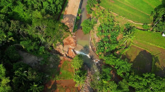 Tilt‑down aerial showing a creek winding through lush greenery as it flows toward the sandy shoreline, with coastal hills and tropical vegetation near Mariveles, Bataan.