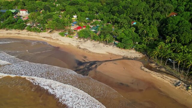Tilt‑down aerial revealing black sand patterns along the shoreline as waves crash onto the coast, framed by lush tropical scenery at Quinawan Beach in Mariveles, Bataan, Philippines.