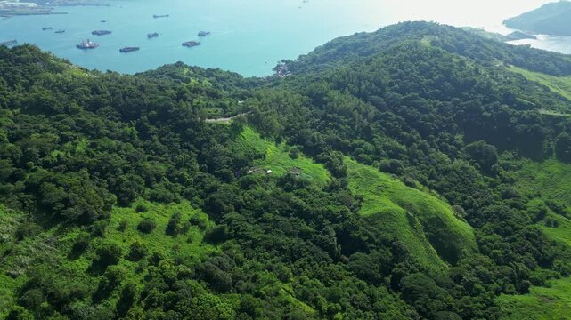 Closing‑in aerial of Nagbayog View Deck in Mariveles, Bataan, moving toward lush green hills and rugged cliffs as the dramatic coastline and turquoise sea are in the background.