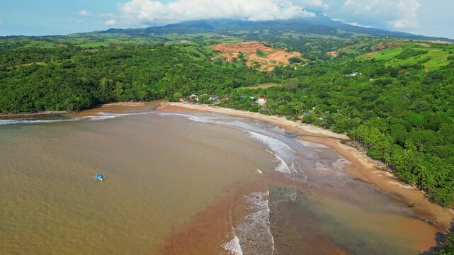 Raised aerial of Quinawan Beach in Mariveles, Bataan, capturing sandy shoreline, brown waters, and lush green hills framing the coastal village and palm‑lined edge.