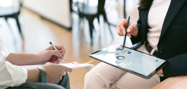 Close-up of two business professionals in formal attire working together, reviewing data on a digital tablet and signing a document.
