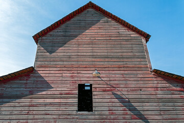 An old lamp casts a shadow on the side of a fading red barn