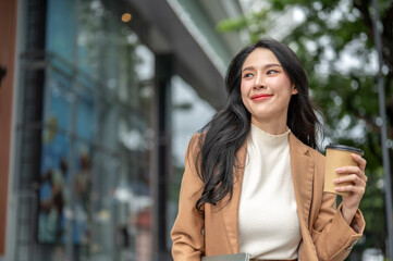 Pretty asian woman office worker holding coffee cup while standing or walking outside shopping mall.
