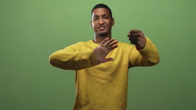 Young black man in yellow sweater gesturing with hands forward, miming holding or steering gesture in studio; welcoming.