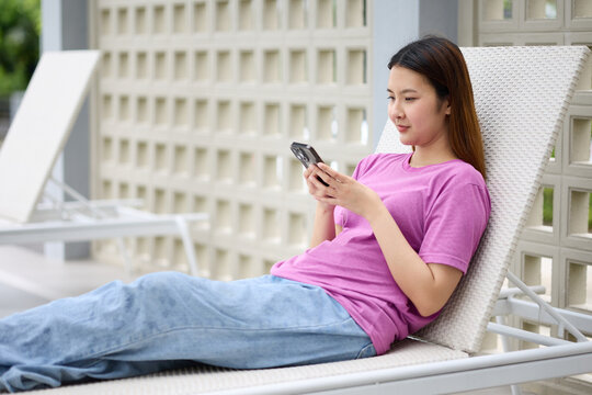 A young woman relaxing on a lounge chair, engrossed in her smartphone
