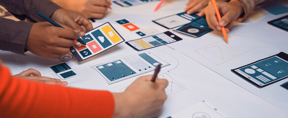 A diverse team collaborates on mobile app design, using colorful markers and sketches on a table. This scene captures creativity and teamwork during the design process. SACTR