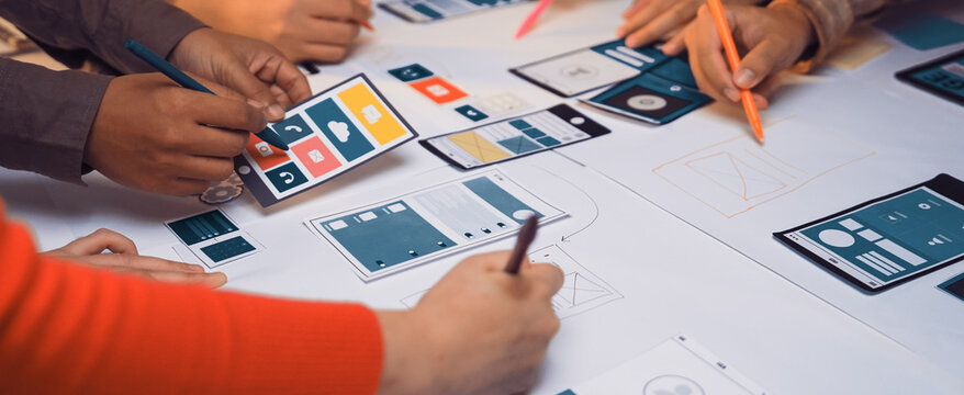 A diverse team collaborates on mobile app design, using colorful markers and sketches on a table. This scene captures creativity and teamwork during the design process. SACTR