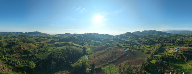 Breathtaking panoramic view of lush green valley under clear blue sky with rolling hills, scattered farmland and distant mountains illuminated by the morning sun.