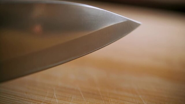 Extreme close up of a sharp steel knife blade tip on a wooden surface.