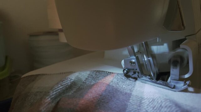 Close-up shot of fabric being sewn on an overlock machine, capturing the precise stitching of the edges. A detailed view of professional garment construction, highlighting craftsmanship and the clean 