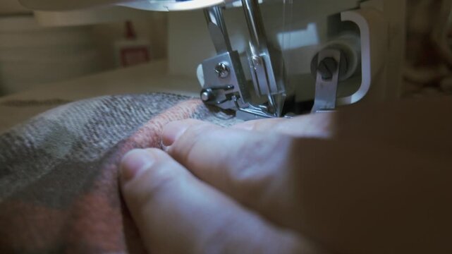 Close-up shot of fabric being sewn on an overlock machine, capturing the precise stitching of the edges. A detailed view of professional garment construction, highlighting craftsmanship and the clean 