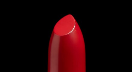 Close up of a vibrant red lipstick bullet with a sharp angled tip against a stark black background