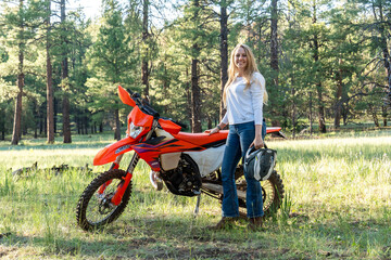 A woman is standing next to a bright dirt bike in a wide open field