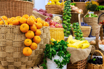 Bright oranges hang from basket among various fruits vegetables in lively market setting.