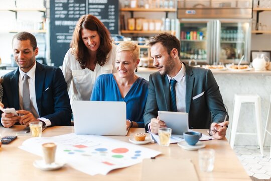 Group of business professionals collaborating in a cafe. Diverse team with laptops and tablets, discussing business plan. Casual business meeting in a modern relaxed restaurant