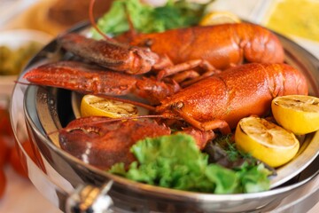 A dish of cooked lobsters with lemon and greens. Lobsters are served on a platter. Fresh lobsters and lemon slices create a vibrant seafood presentation. Cooked lobster, party food.