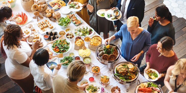Diverse group enjoying buffet with various dishes. People gather around a table filled with food. Buffet includes salads, meats, and desserts. Social dining scene. People at dinner buffet together.